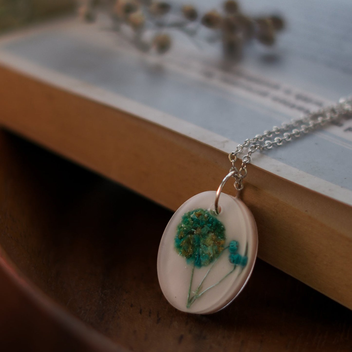 A collection of handmade resin art pendants, showcasing intricate floral designs preserved in clear resin, attached to delicate necklaces.
