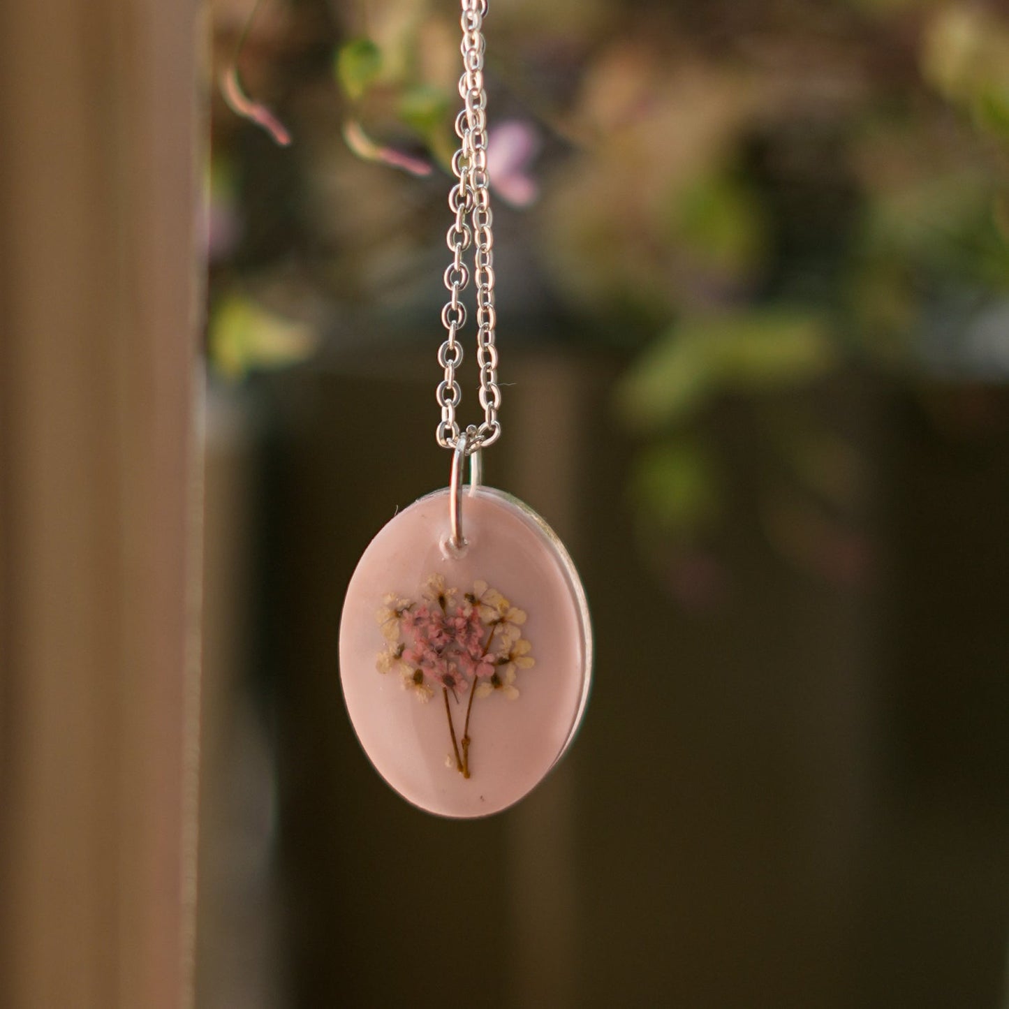 A collection of handmade resin art pendants, showcasing intricate floral designs preserved in clear resin, attached to delicate necklaces.