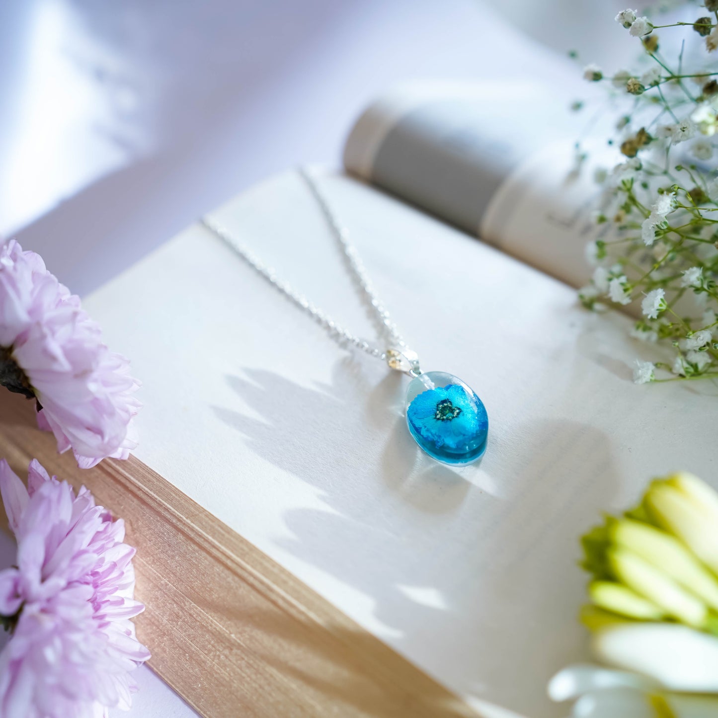 A collection of handmade resin art pendants, showcasing intricate floral designs preserved in clear resin, attached to delicate necklaces.