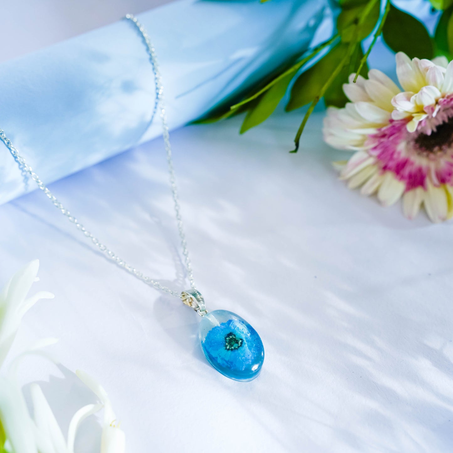 A collection of handmade resin art pendants, showcasing intricate floral designs preserved in clear resin, attached to delicate necklaces.