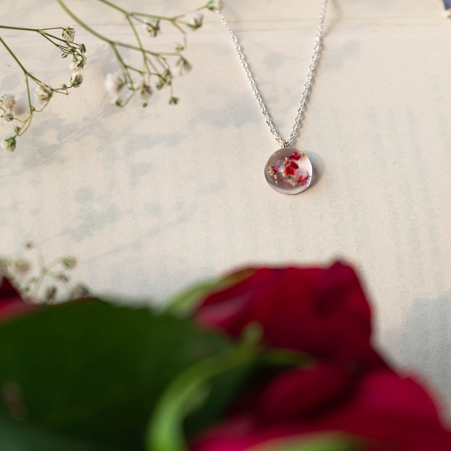 A collection of handmade resin art pendants, showcasing intricate floral designs preserved in clear resin, attached to delicate necklaces.