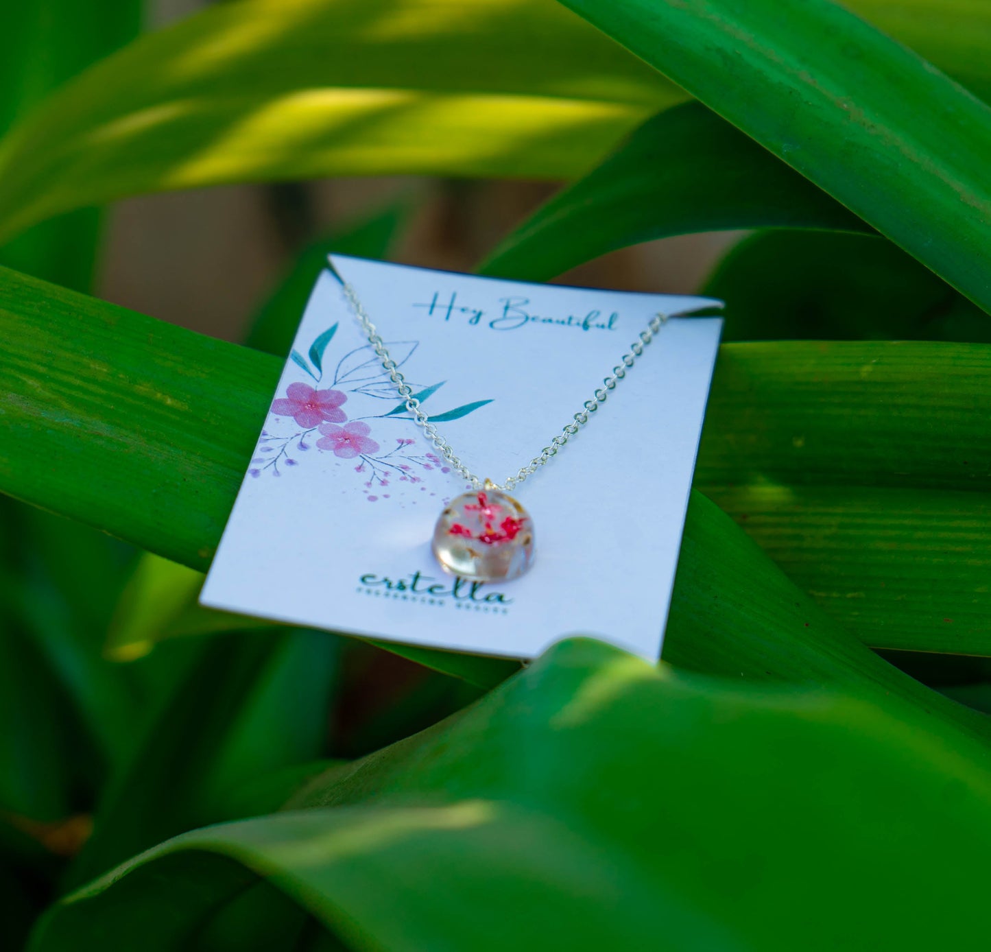 A collection of handmade resin art pendants, showcasing intricate floral designs preserved in clear resin, attached to delicate necklaces.