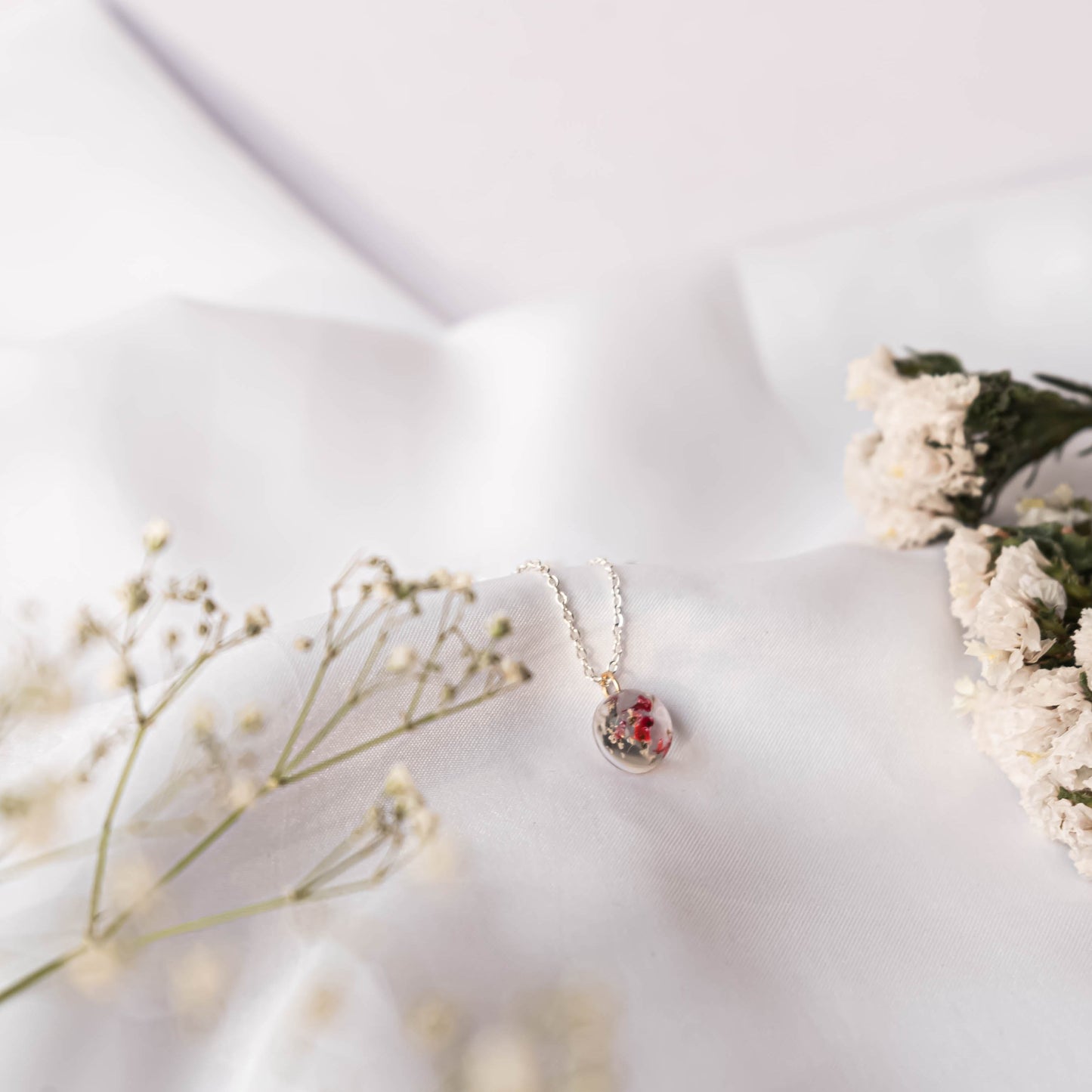 A collection of handmade resin art pendants, showcasing intricate floral designs preserved in clear resin, attached to delicate necklaces.