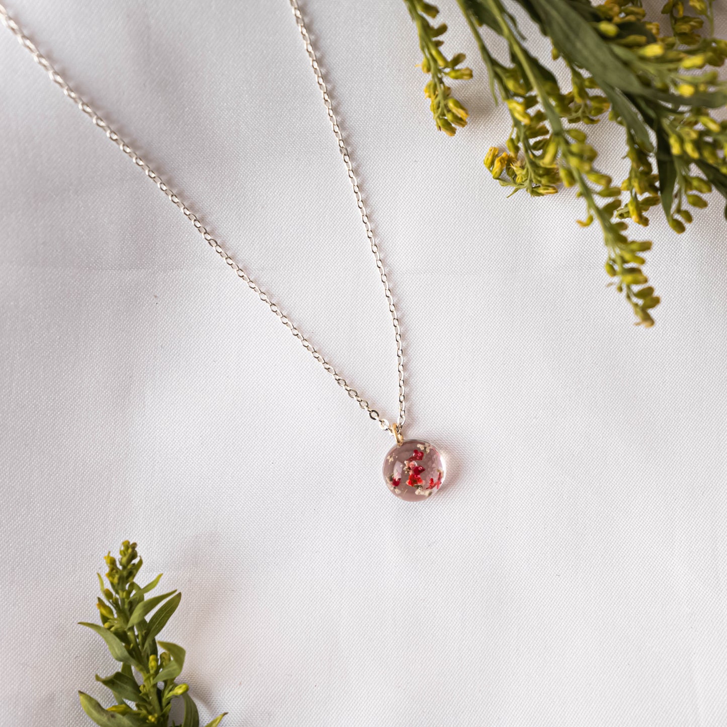 A collection of handmade resin art pendants, showcasing intricate floral designs preserved in clear resin, attached to delicate necklaces.