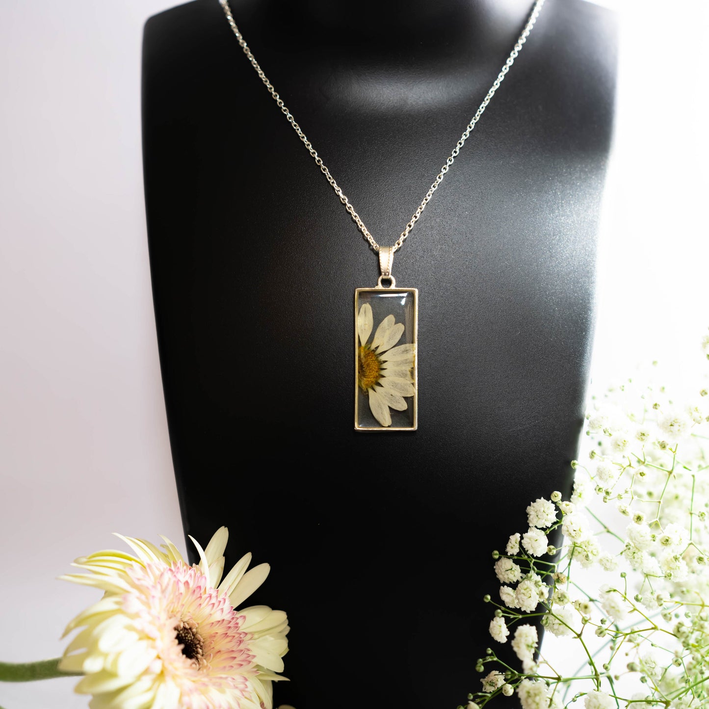 A collection of handmade resin art pendants, showcasing intricate floral designs preserved in clear resin, attached to delicate necklaces.