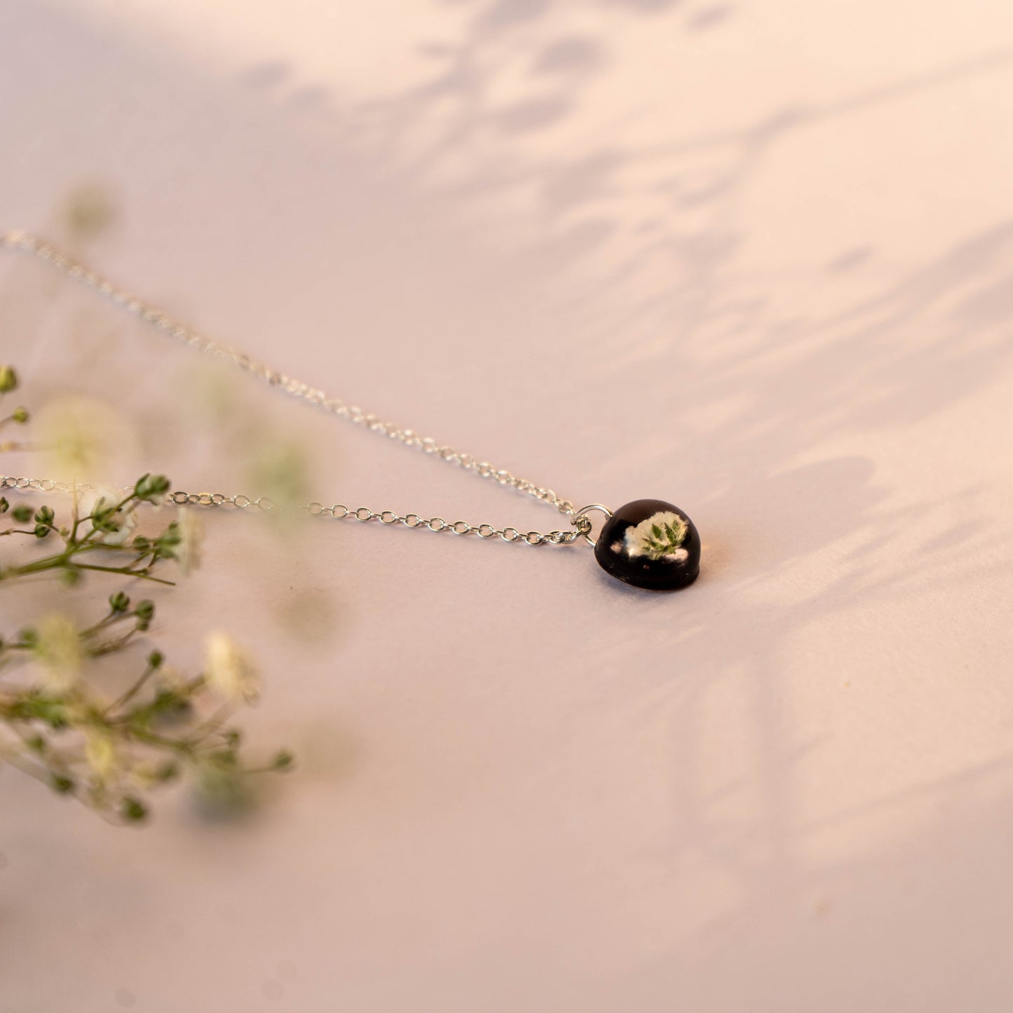A collection of handmade resin art pendants, showcasing intricate floral designs preserved in clear resin, attached to delicate necklaces.