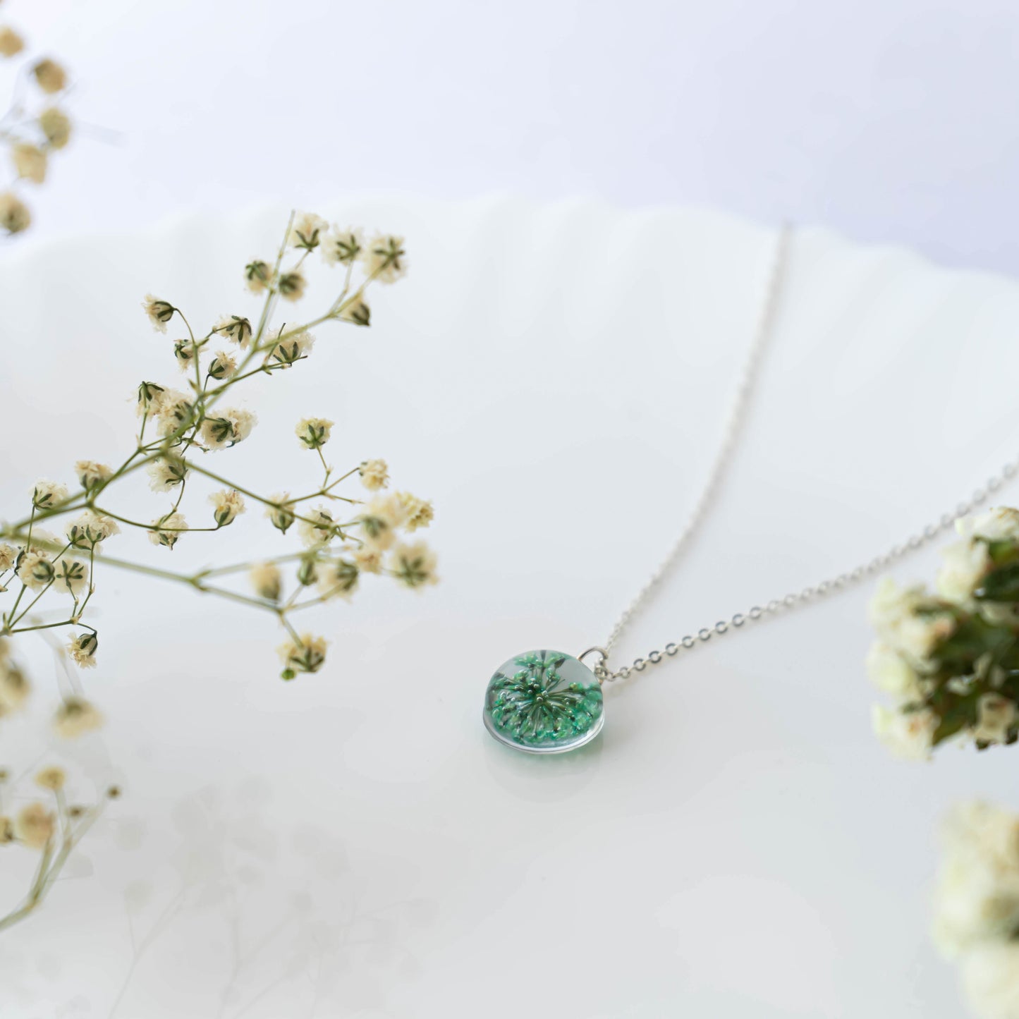 A collection of handmade resin art pendants, showcasing intricate floral designs preserved in clear resin, attached to delicate necklaces.