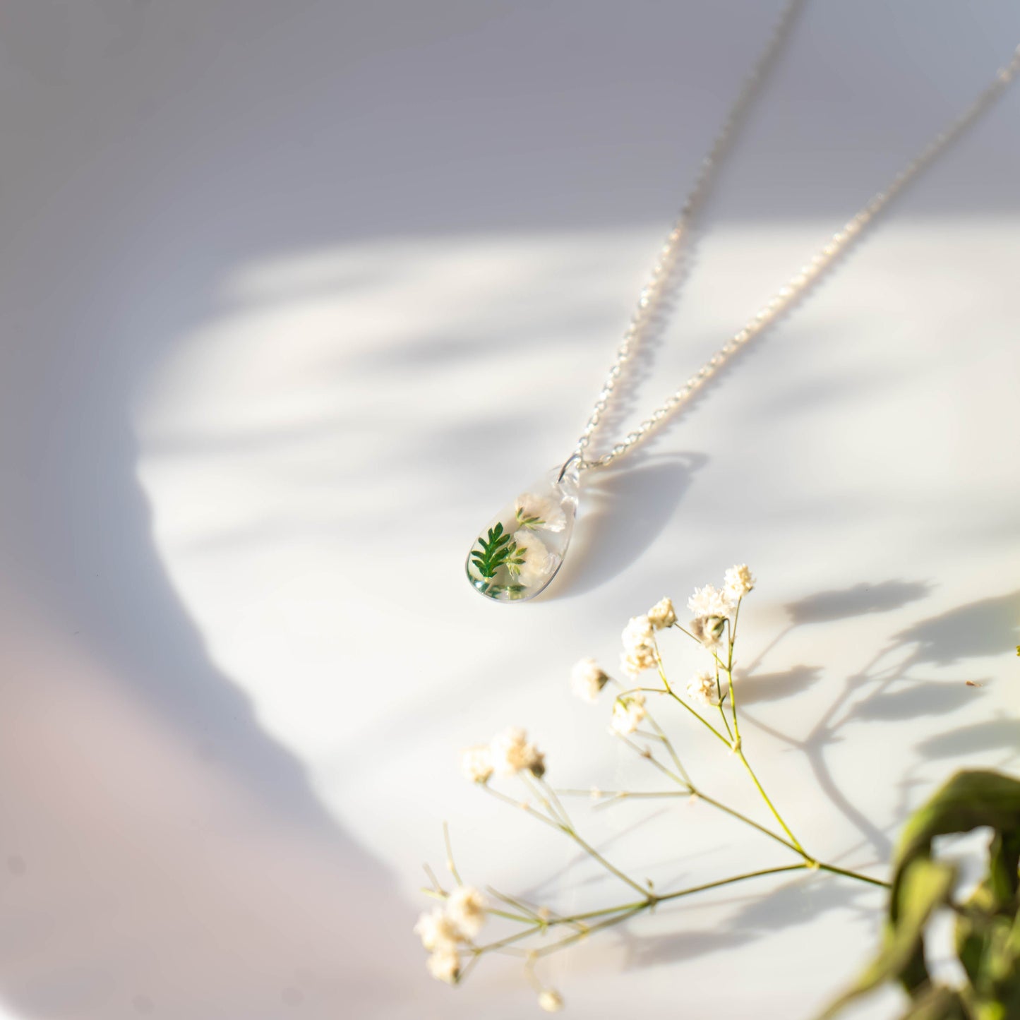 A collection of handmade resin art pendants, showcasing intricate floral designs preserved in clear resin, attached to delicate necklaces.