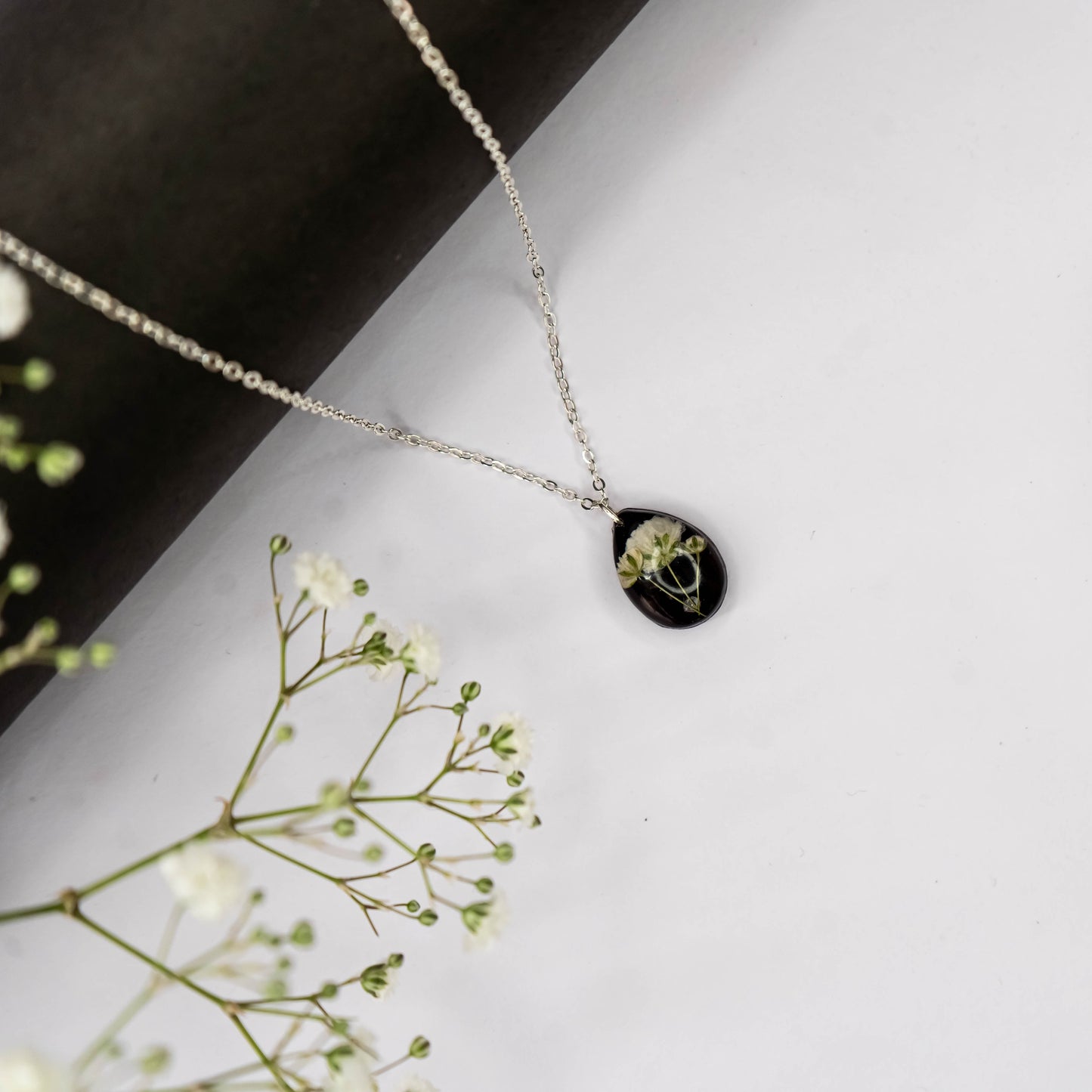 A collection of handmade resin art pendants, showcasing intricate floral designs preserved in clear resin, attached to delicate necklaces.