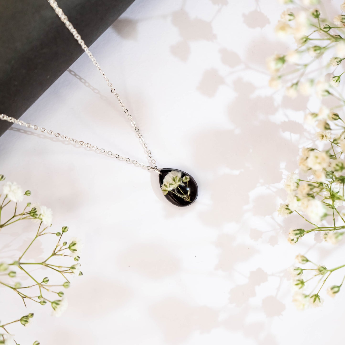 A collection of handmade resin art pendants, showcasing intricate floral designs preserved in clear resin, attached to delicate necklaces.