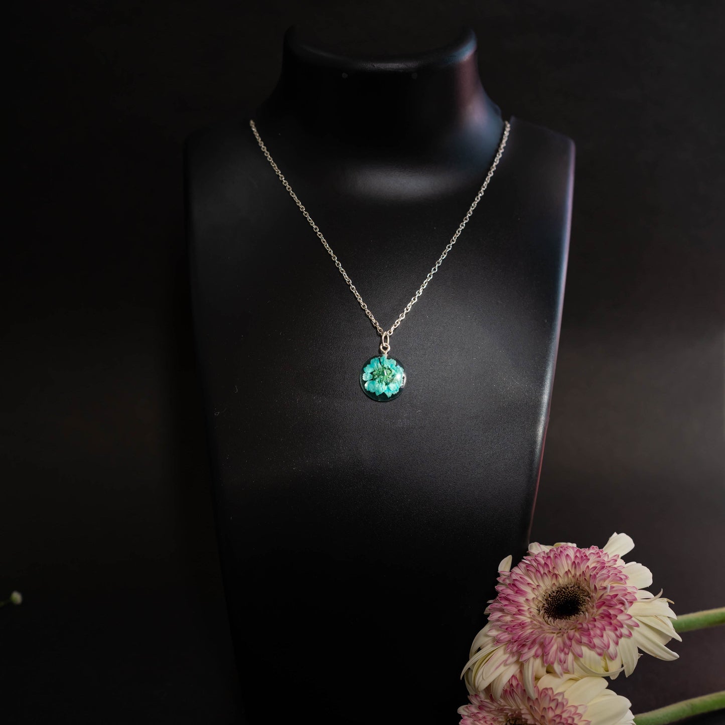 A collection of handmade resin art pendants, showcasing intricate floral designs preserved in clear resin, attached to delicate necklaces.