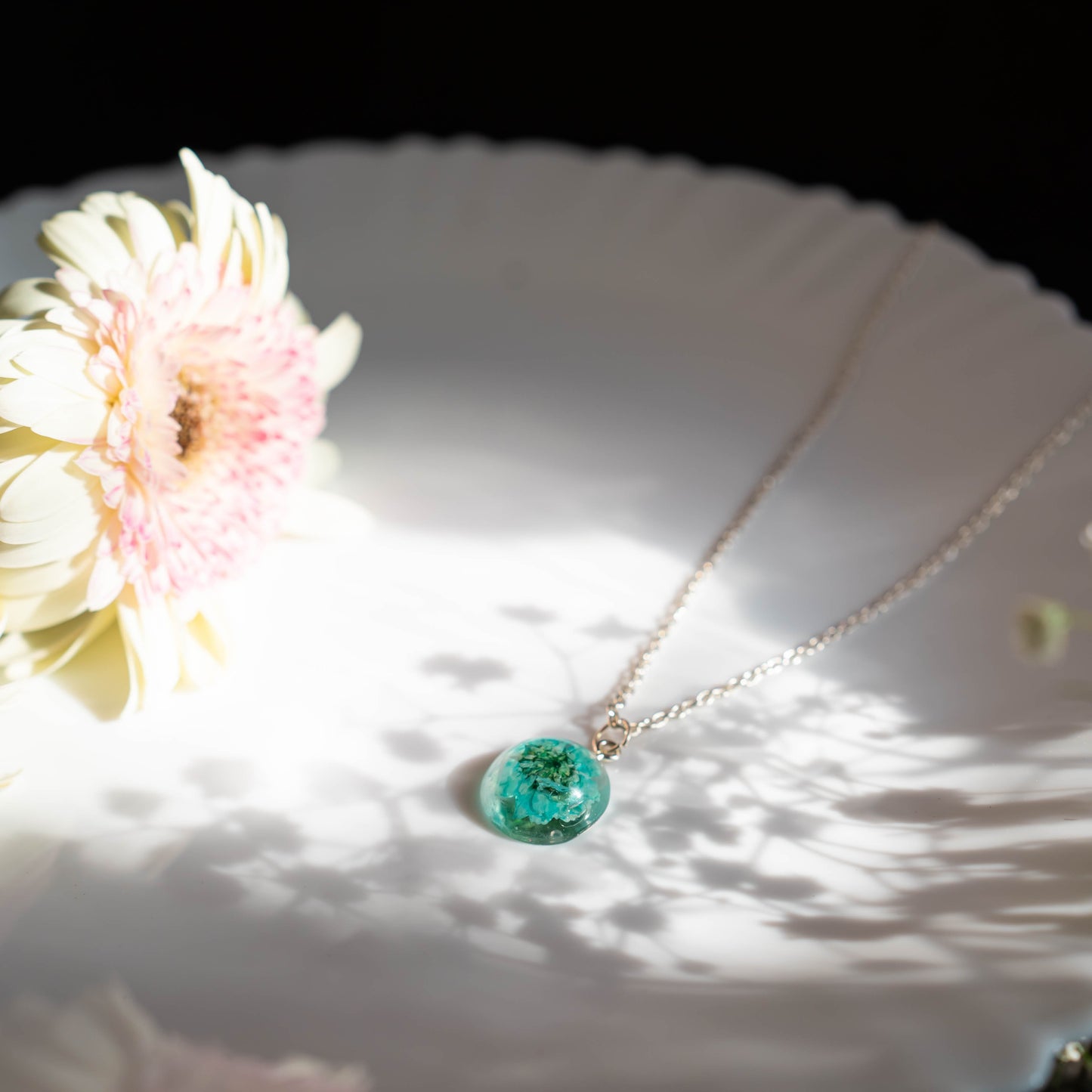 A collection of handmade resin art pendants, showcasing intricate floral designs preserved in clear resin, attached to delicate necklaces.