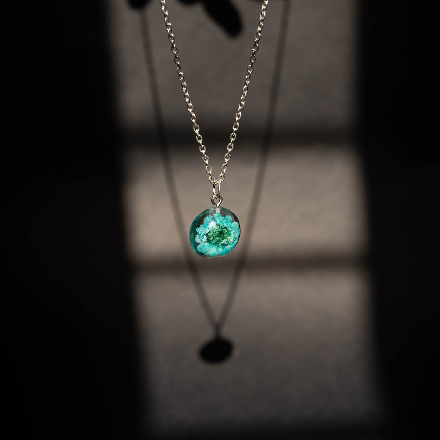 A collection of handmade resin art pendants, showcasing intricate floral designs preserved in clear resin, attached to delicate necklaces.