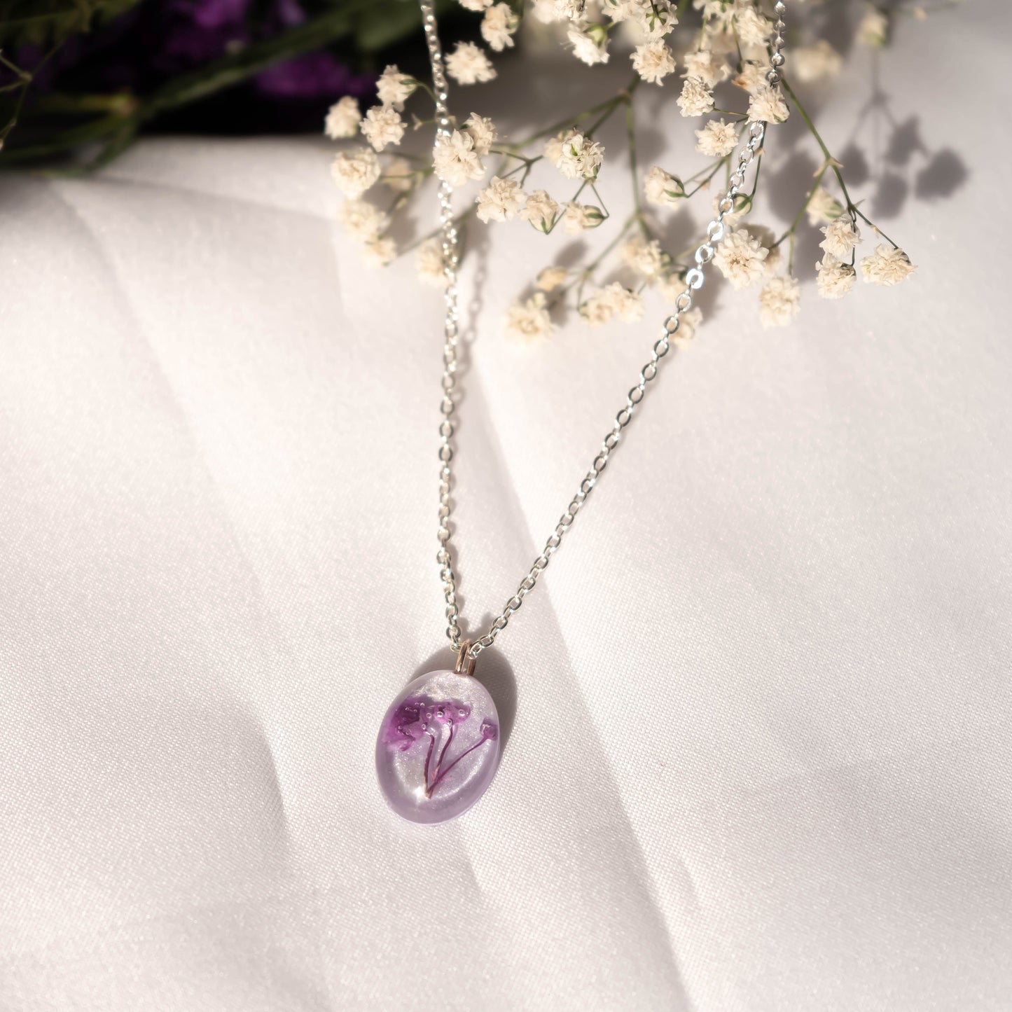 A collection of handmade resin art pendants, showcasing intricate floral designs preserved in clear resin, attached to delicate necklaces.