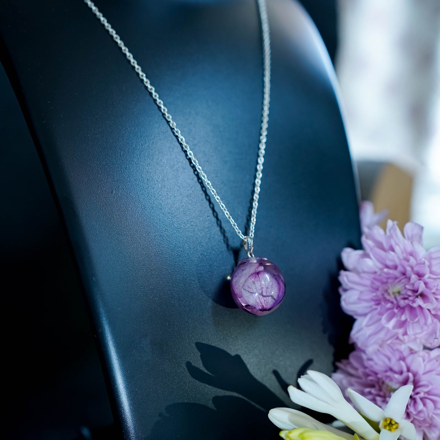 A collection of handmade resin art pendants, showcasing intricate floral designs preserved in clear resin, attached to delicate necklaces.