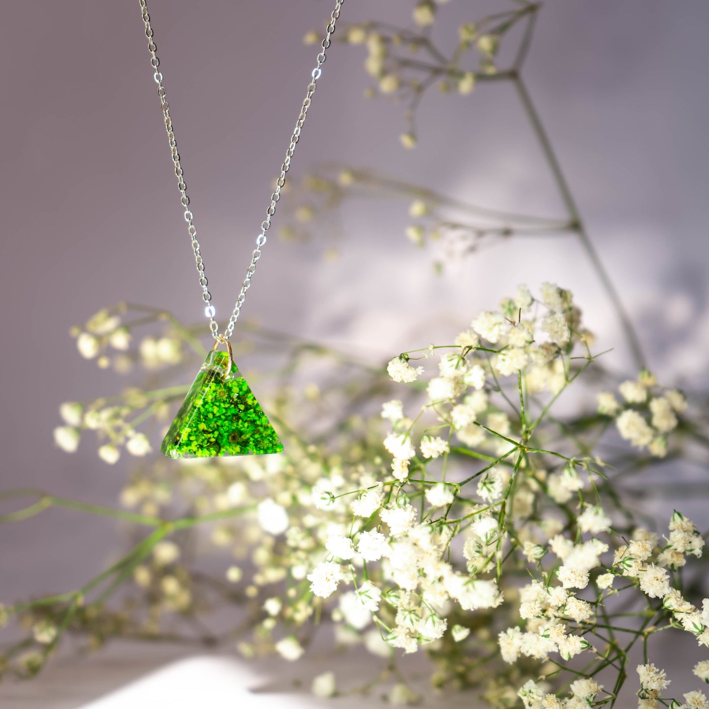 A collection of handmade resin art pendants, showcasing intricate floral designs preserved in clear resin, attached to delicate necklaces.