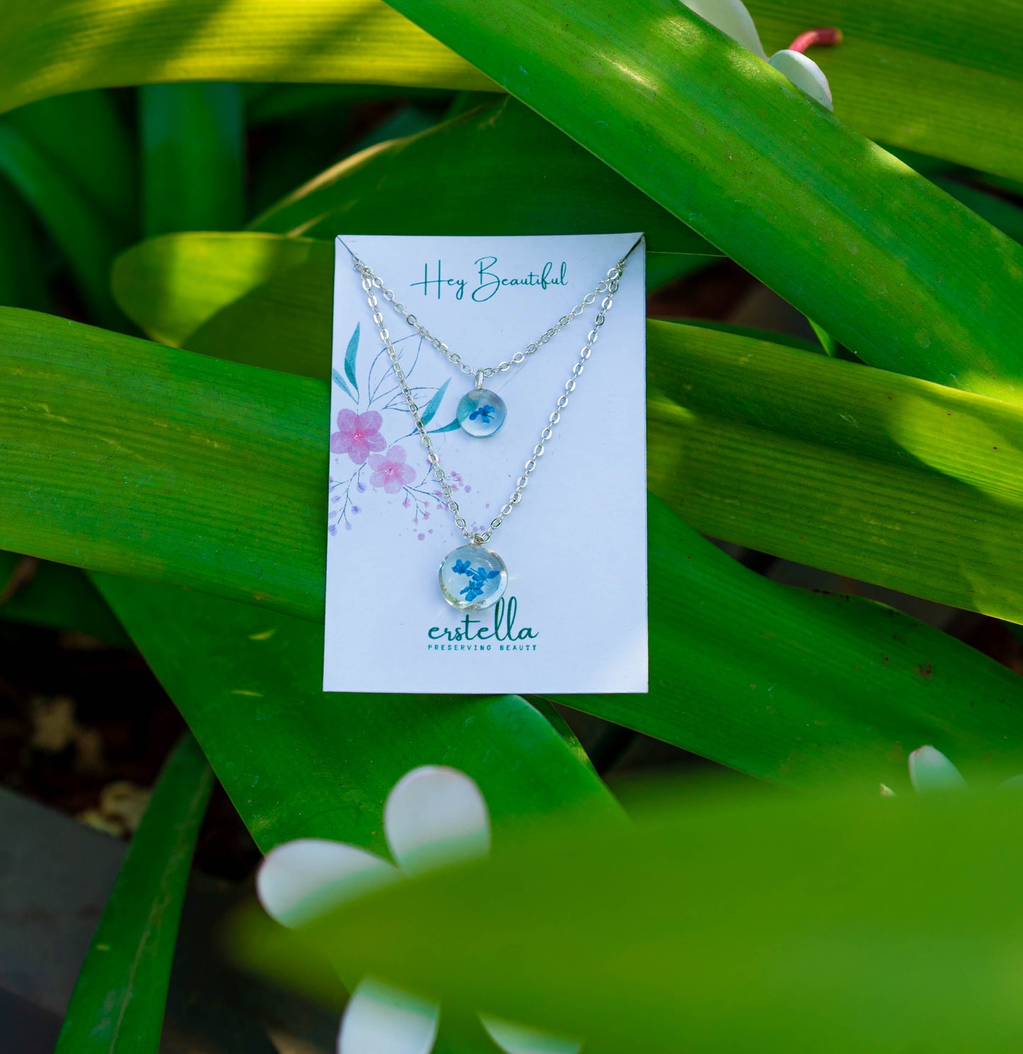 A collection of handmade resin art pendants, showcasing intricate floral designs preserved in clear resin, attached to delicate necklaces.