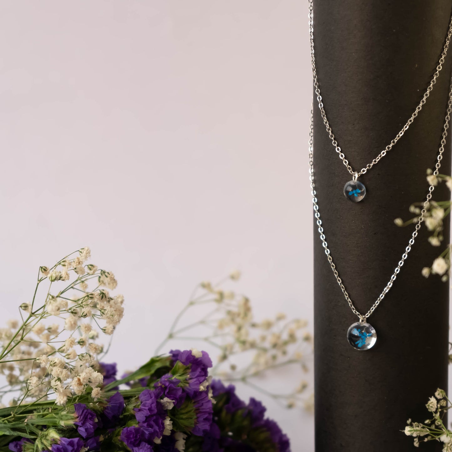 A collection of handmade resin art pendants, showcasing intricate floral designs preserved in clear resin, attached to delicate necklaces.