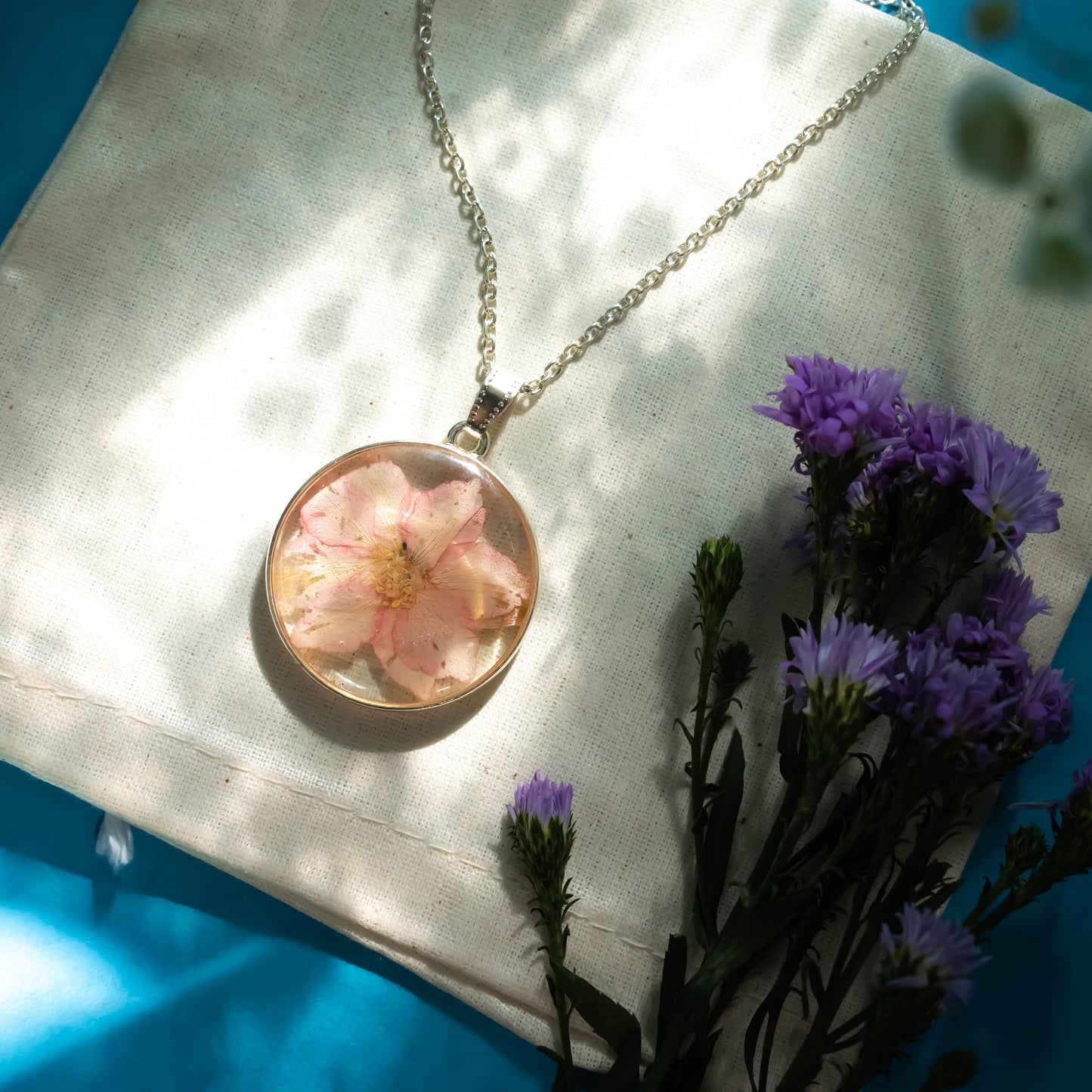A collection of handmade resin art pendants, showcasing intricate floral designs preserved in clear resin, attached to delicate necklaces.