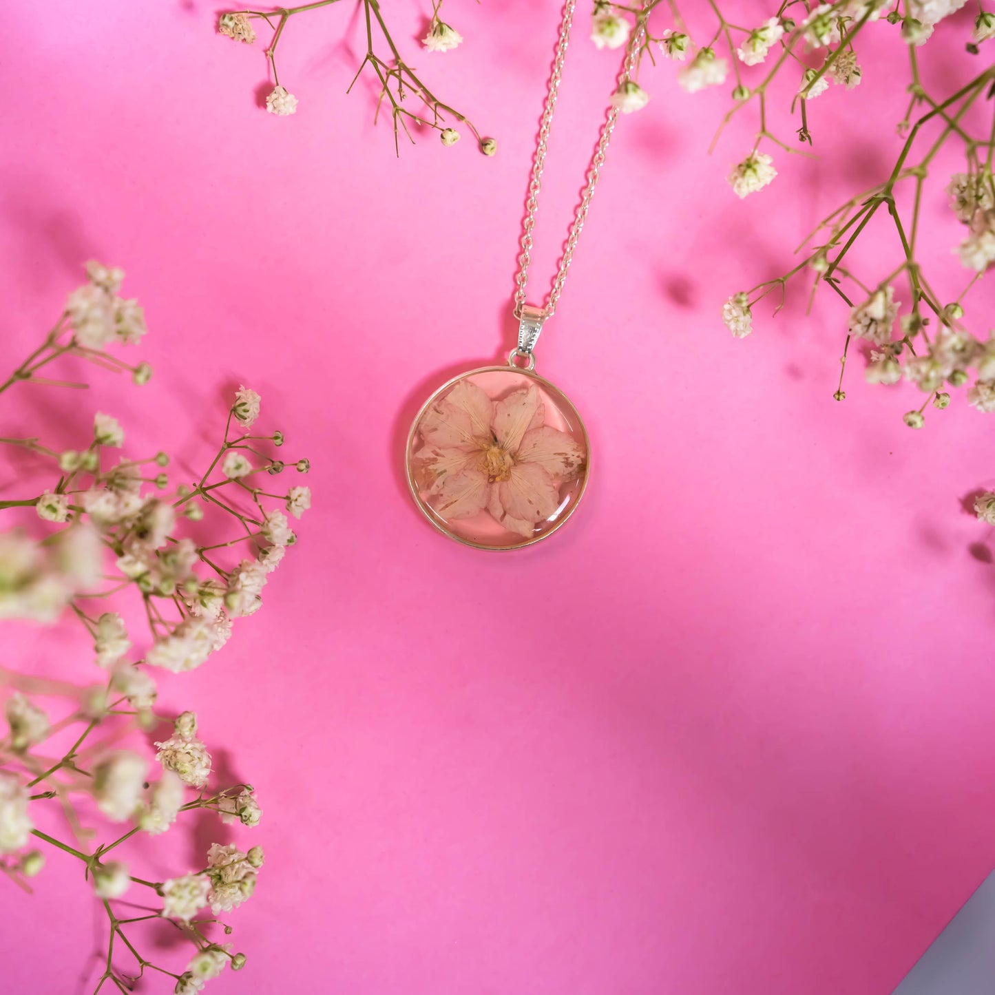 A collection of handmade resin art pendants, showcasing intricate floral designs preserved in clear resin, attached to delicate necklaces.