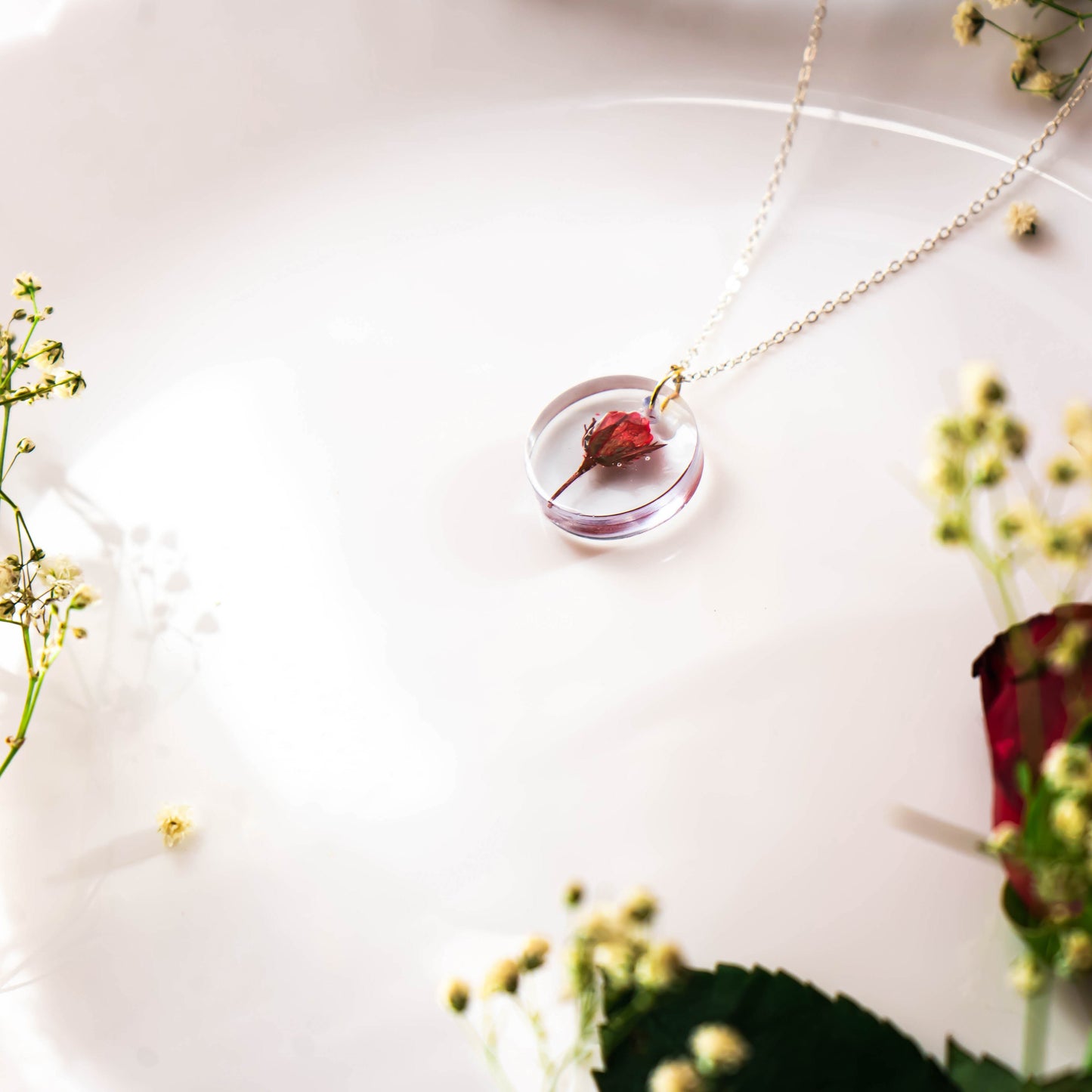 A collection of handmade resin art pendants, showcasing intricate floral designs preserved in clear resin, attached to delicate necklaces.