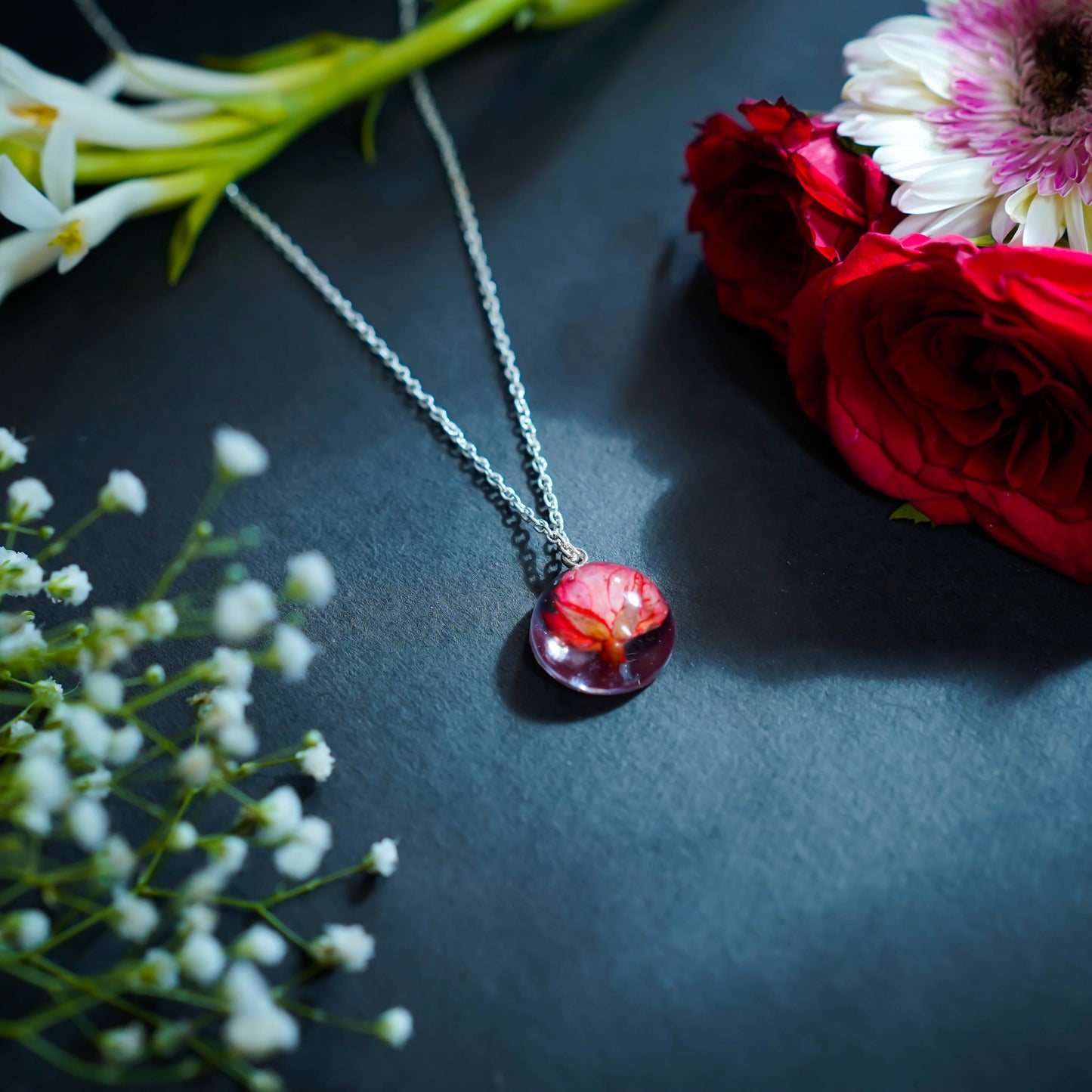 A collection of handmade resin art pendants, showcasing intricate floral designs preserved in clear resin, attached to delicate necklaces.