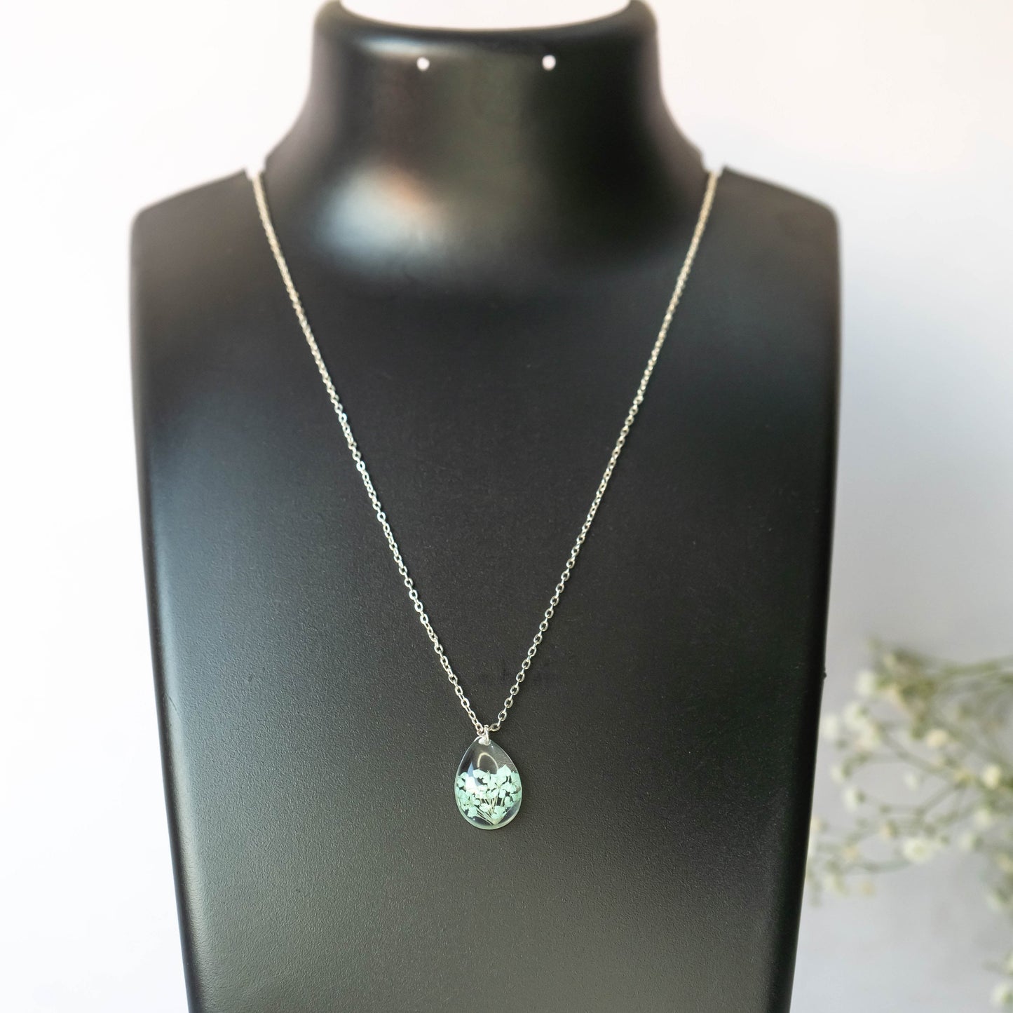 A collection of handmade resin art pendants, showcasing intricate floral designs preserved in clear resin, attached to delicate necklaces.