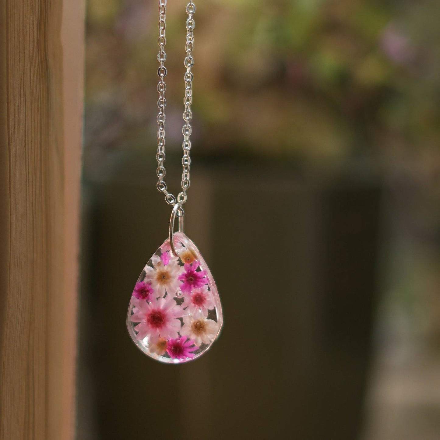 A collection of handmade resin art pendants, showcasing intricate floral designs preserved in clear resin, attached to delicate necklaces.