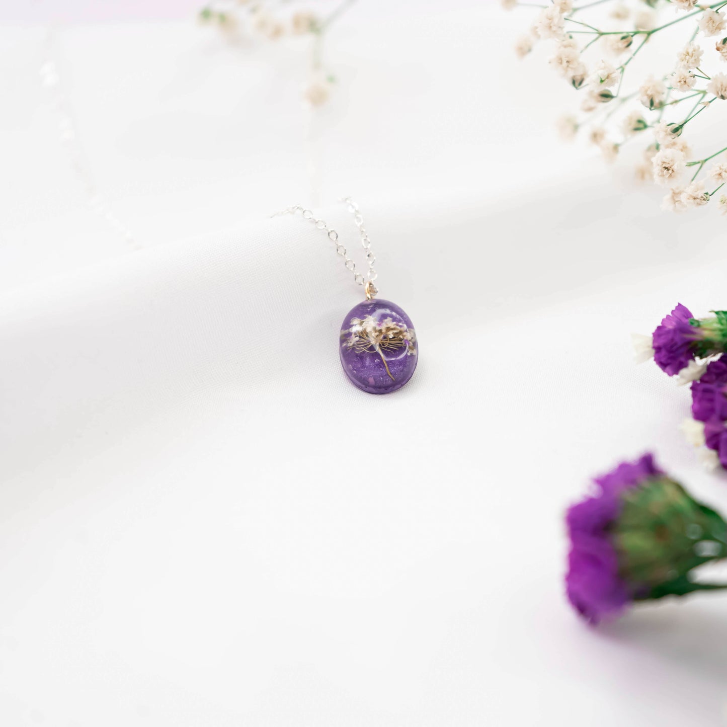 A collection of handmade resin art pendants, showcasing intricate floral designs preserved in clear resin, attached to delicate necklaces.