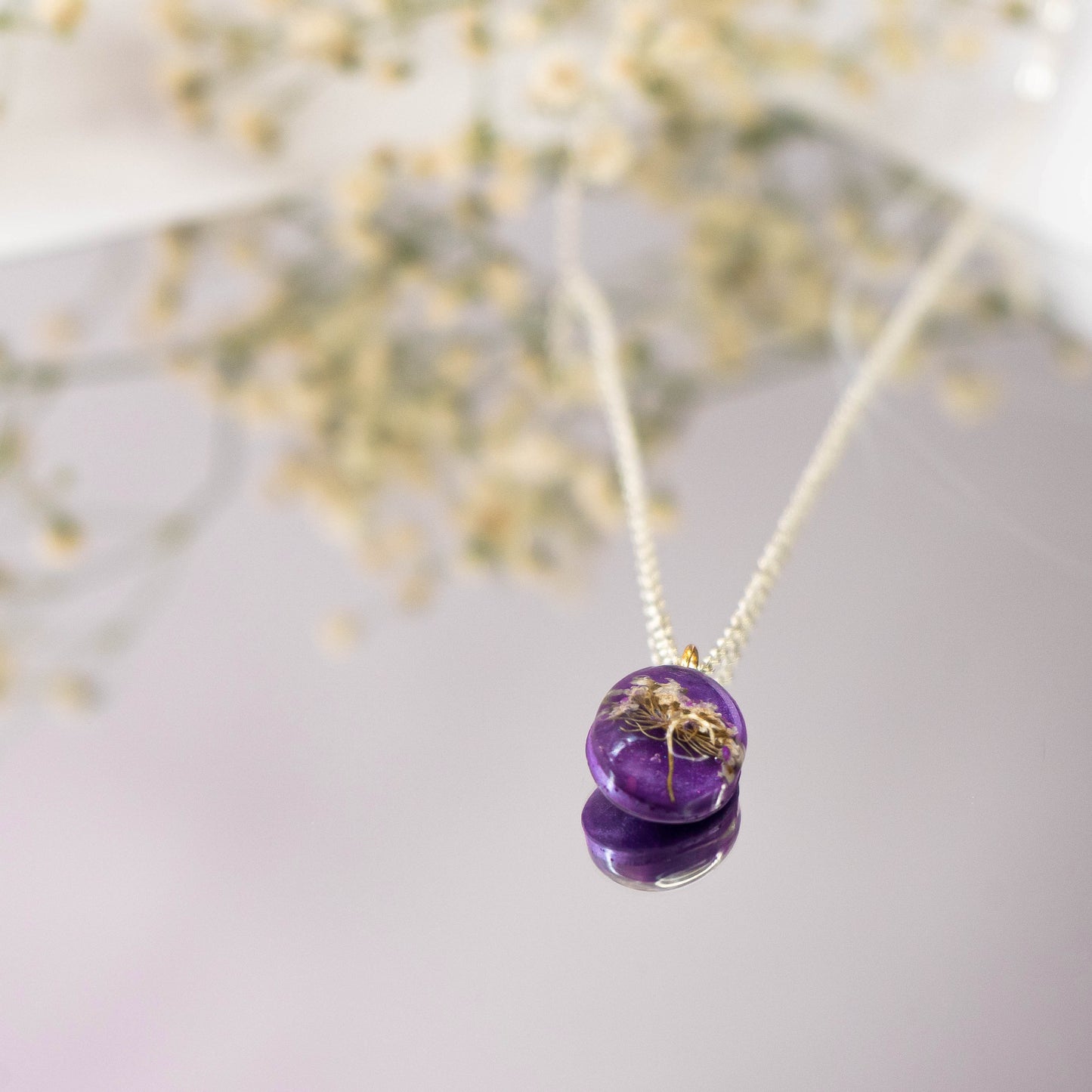 A collection of handmade resin art pendants, showcasing intricate floral designs preserved in clear resin, attached to delicate necklaces.