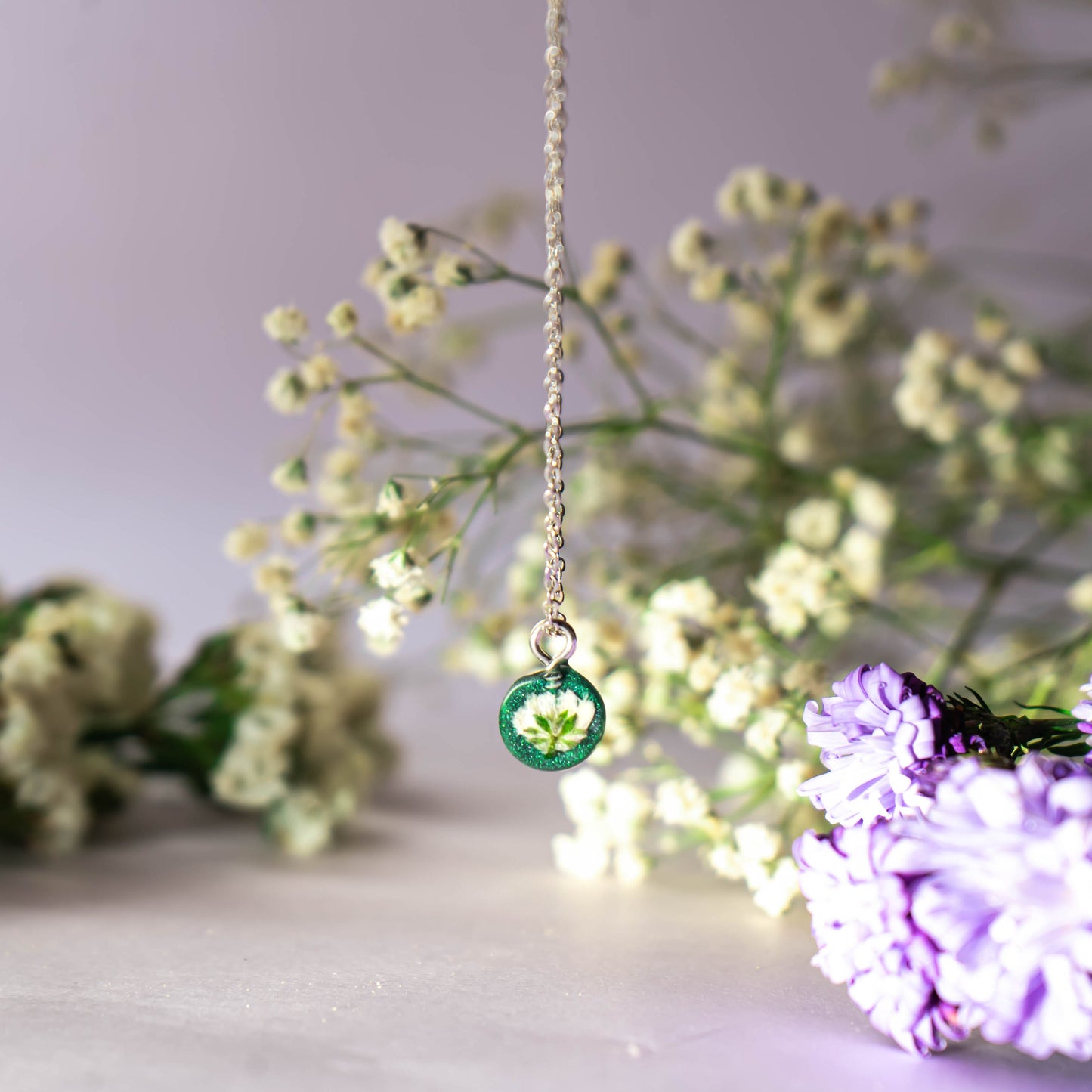 A collection of handmade resin art pendants, showcasing intricate floral designs preserved in clear resin, attached to delicate necklaces.