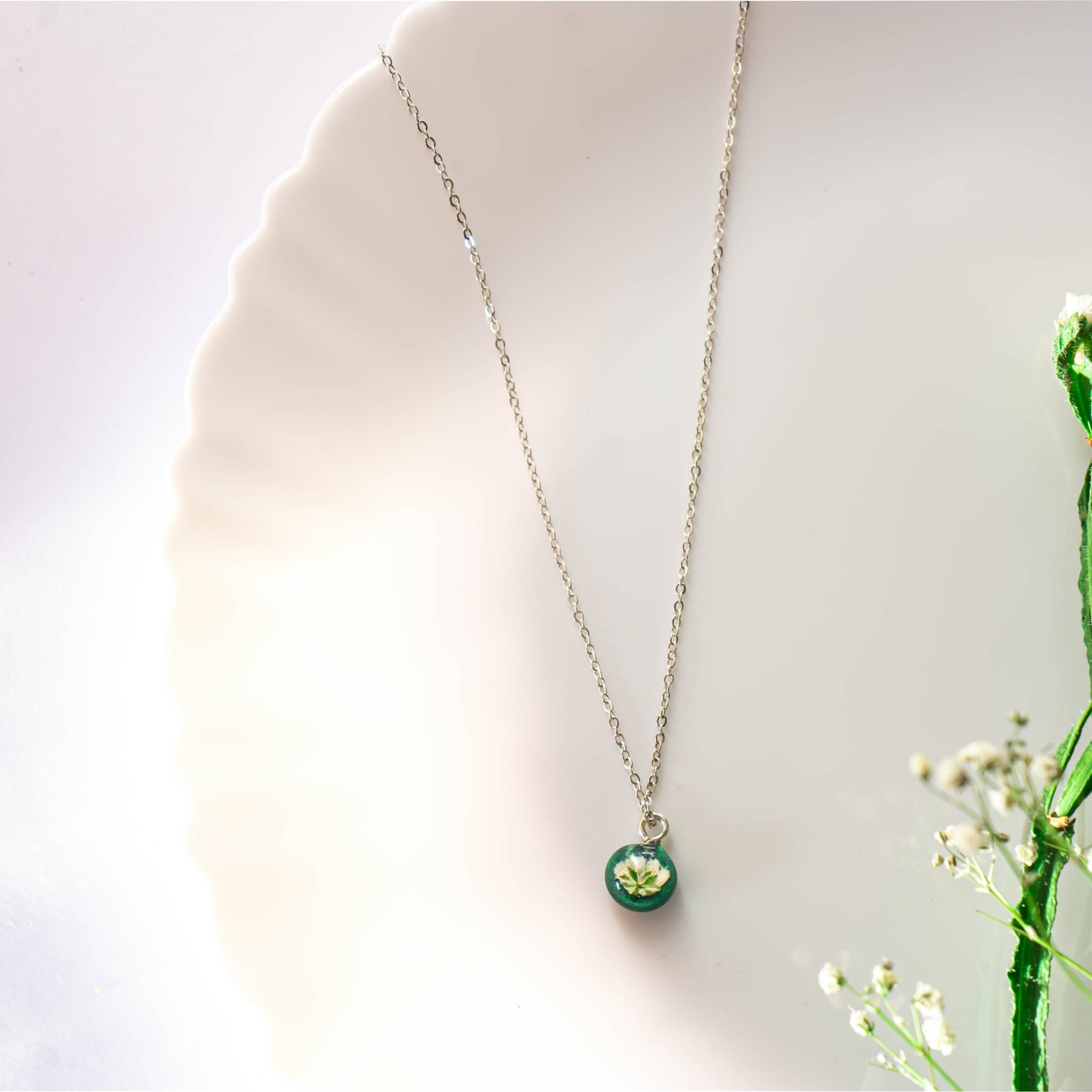 A collection of handmade resin art pendants, showcasing intricate floral designs preserved in clear resin, attached to delicate necklaces.