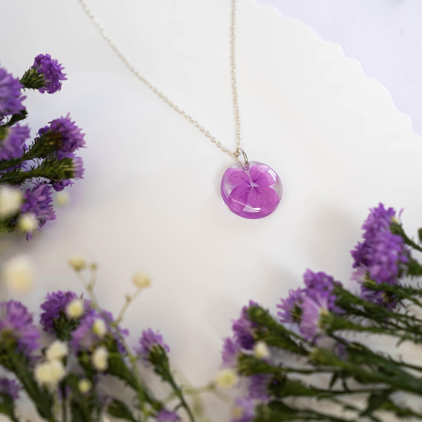 A collection of handmade resin art pendants, showcasing intricate floral designs preserved in clear resin, attached to delicate necklaces.