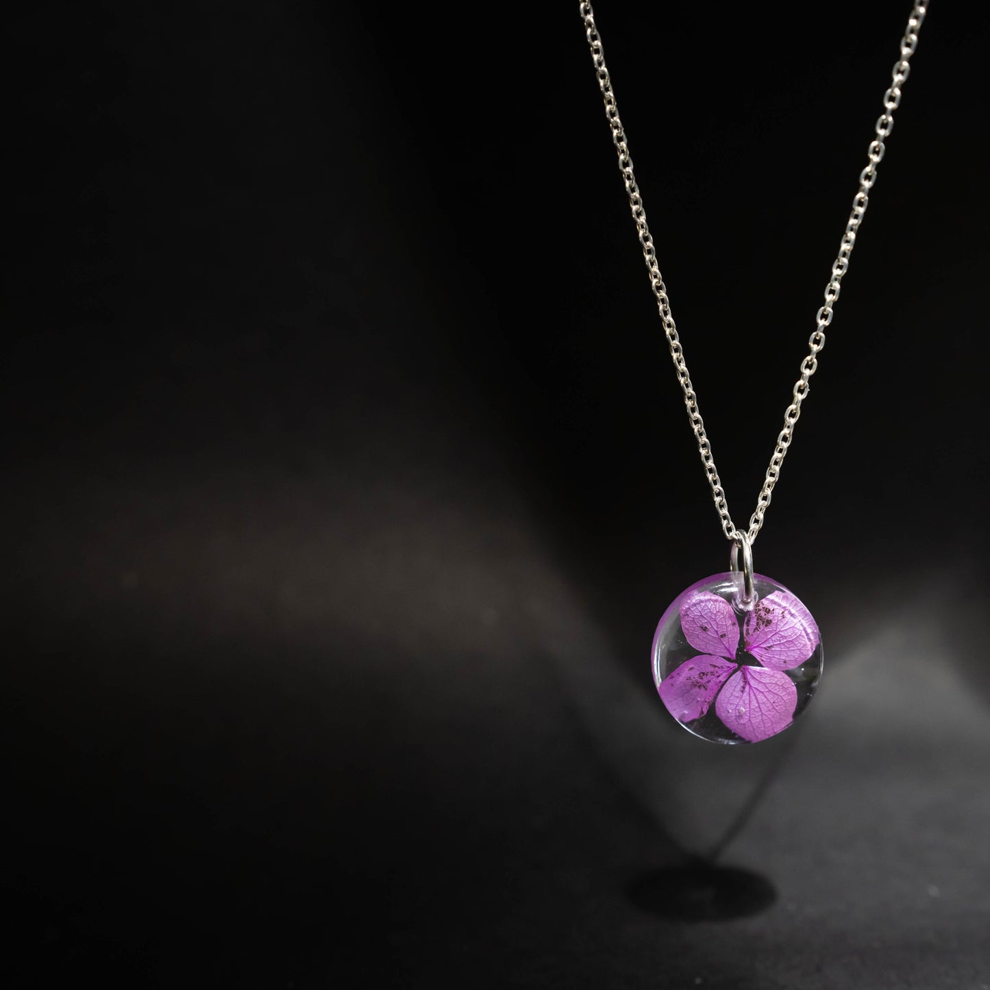 A collection of handmade resin art pendants, showcasing intricate floral designs preserved in clear resin, attached to delicate necklaces.