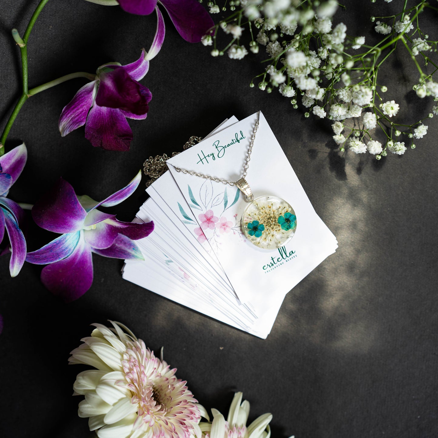 A collection of handmade resin art pendants, showcasing intricate floral designs preserved in clear resin, attached to delicate necklaces.