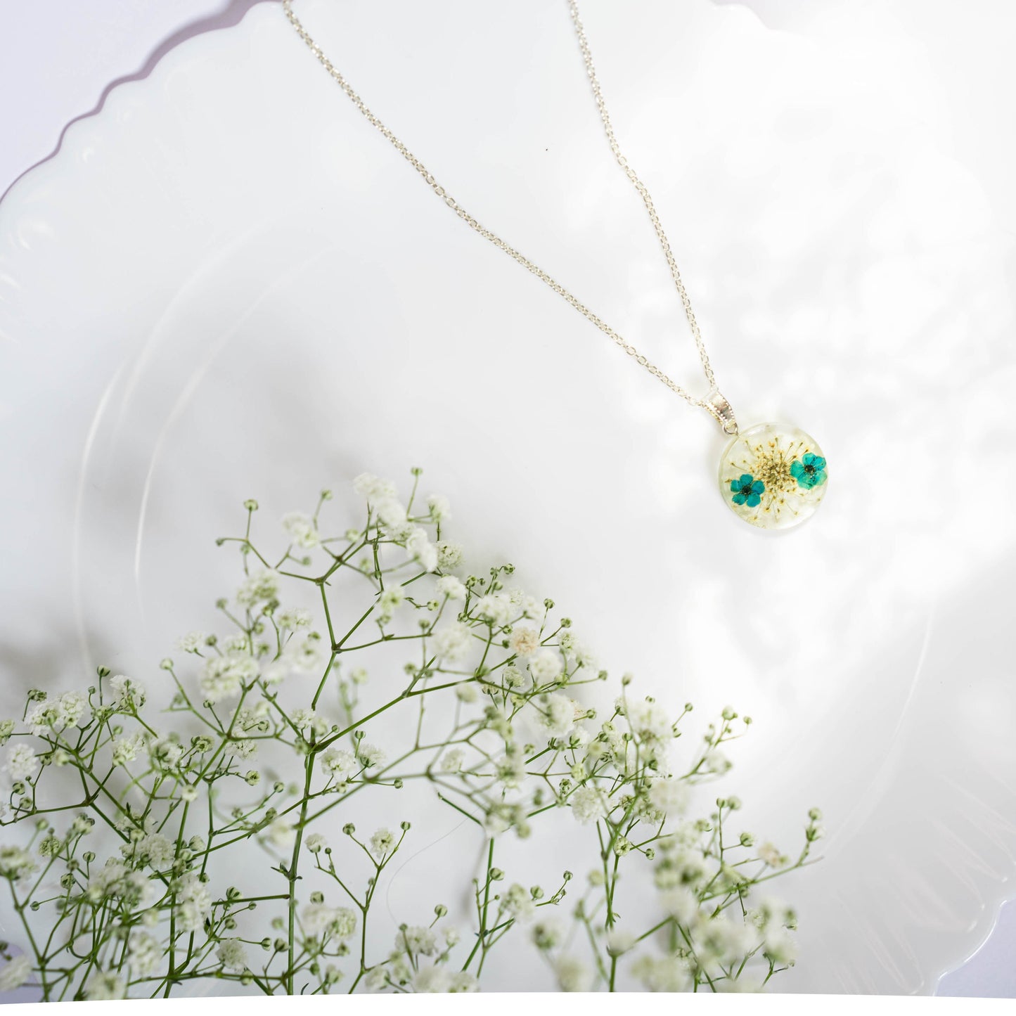 A collection of handmade resin art pendants, showcasing intricate floral designs preserved in clear resin, attached to delicate necklaces.