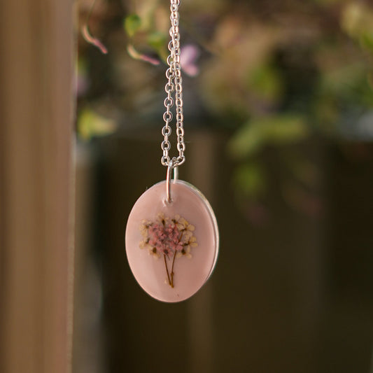 A collection of handmade resin art pendants, showcasing intricate floral designs preserved in clear resin, attached to delicate necklaces.