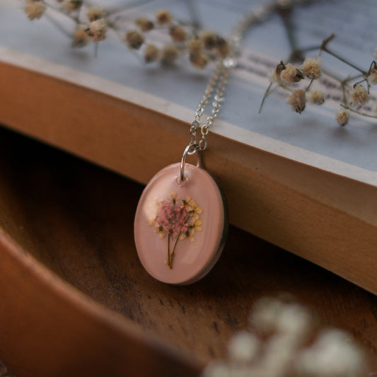 A collection of handmade resin art pendants, showcasing intricate floral designs preserved in clear resin, attached to delicate necklaces.