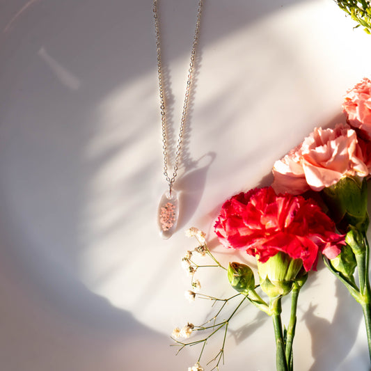 A collection of handmade resin art pendants, showcasing intricate floral designs preserved in clear resin, attached to delicate necklaces.