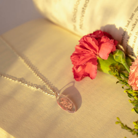 A collection of handmade resin art pendants, showcasing intricate floral designs preserved in clear resin, attached to delicate necklaces.