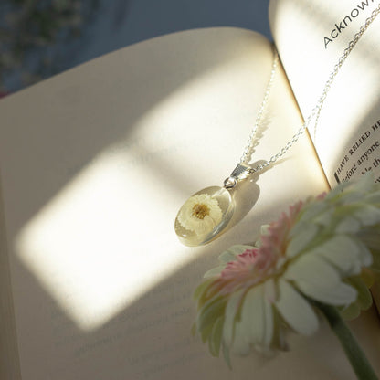 A collection of handmade resin art pendants, showcasing intricate floral designs preserved in clear resin, attached to delicate necklaces.