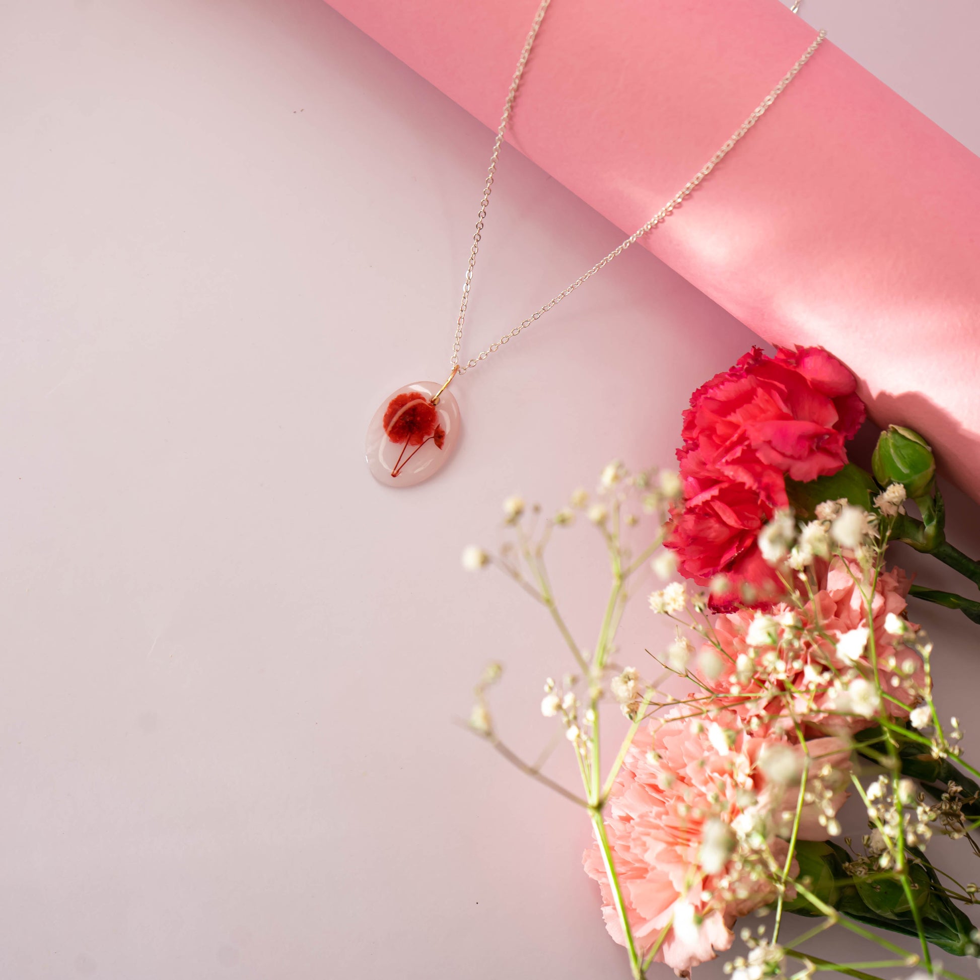 A collection of handmade resin art pendants, showcasing intricate floral designs preserved in clear resin, attached to delicate necklaces.