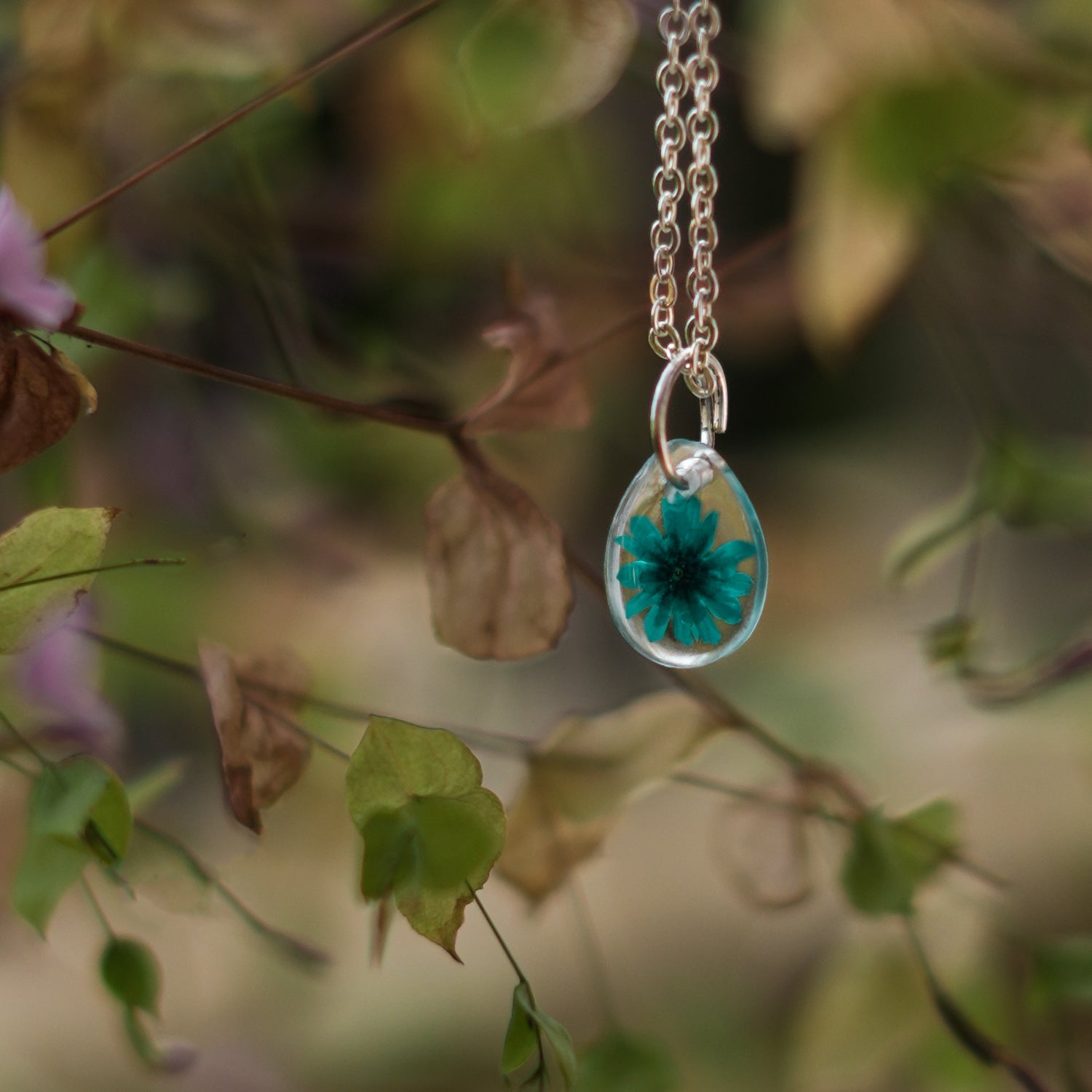 A collection of handmade resin art pendants, showcasing intricate floral designs preserved in clear resin, attached to delicate necklaces.