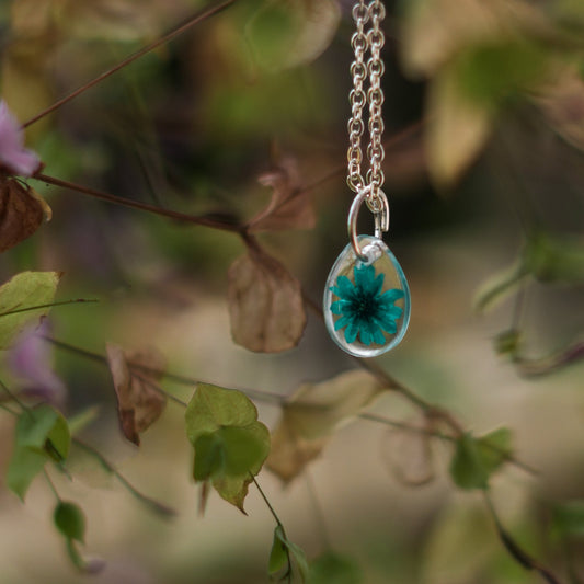 A collection of handmade resin art pendants, showcasing intricate floral designs preserved in clear resin, attached to delicate necklaces.