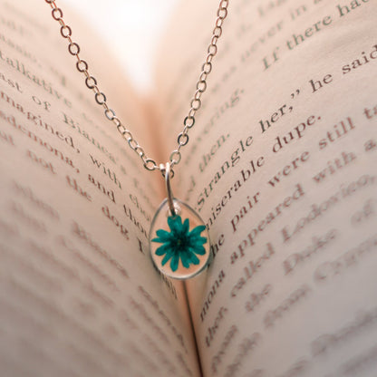 A collection of handmade resin art pendants, showcasing intricate floral designs preserved in clear resin, attached to delicate necklaces.