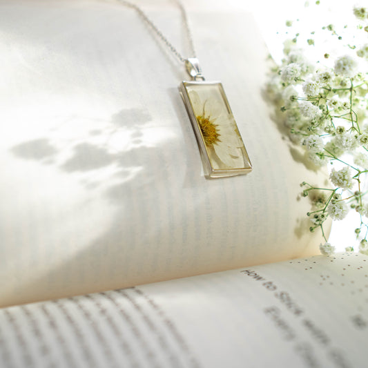 A collection of handmade resin art pendants, showcasing intricate floral designs preserved in clear resin, attached to delicate necklaces.