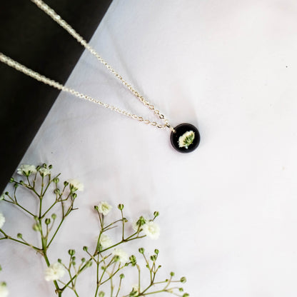 A collection of handmade resin art pendants, showcasing intricate floral designs preserved in clear resin, attached to delicate necklaces.
