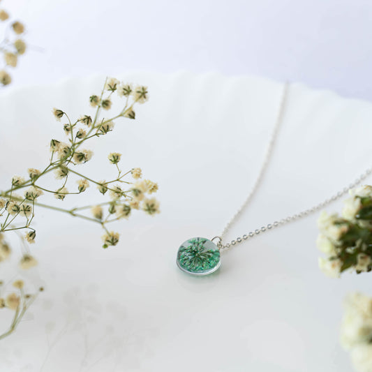A collection of handmade resin art pendants, showcasing intricate floral designs preserved in clear resin, attached to delicate necklaces.
