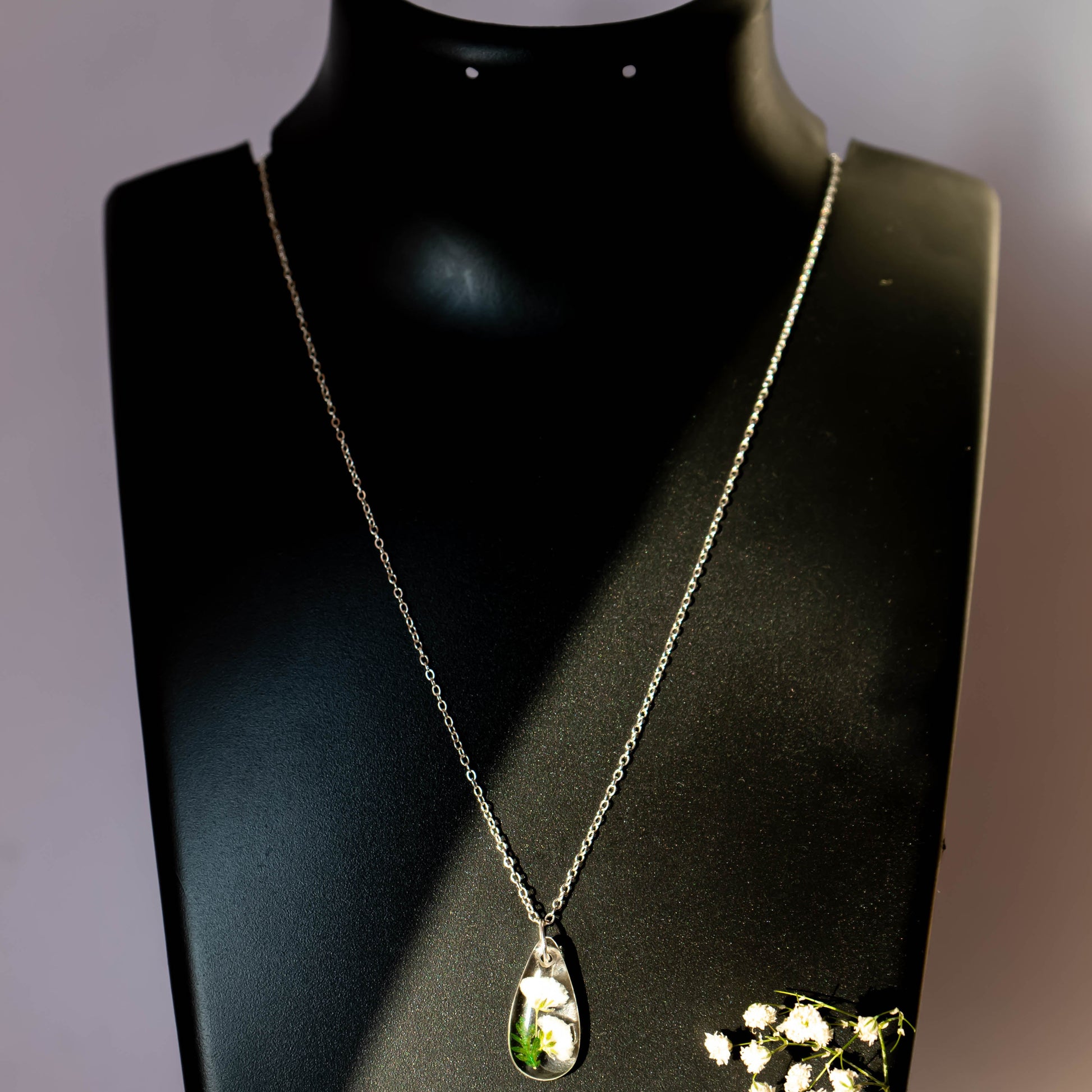 A collection of handmade resin art pendants, showcasing intricate floral designs preserved in clear resin, attached to delicate necklaces.