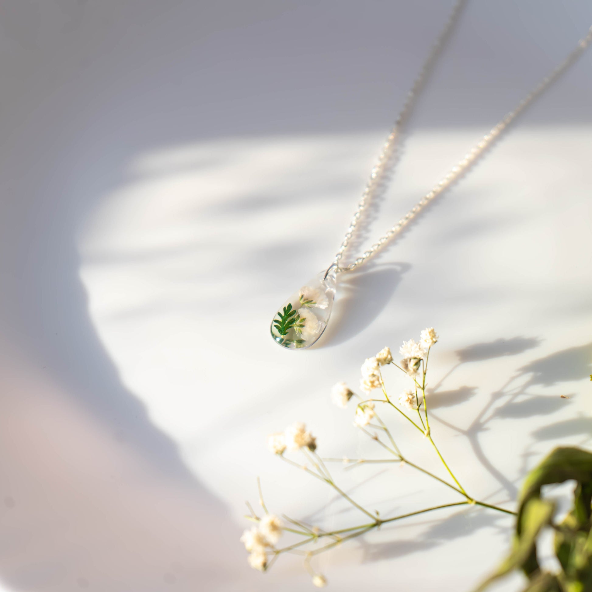 A collection of handmade resin art pendants, showcasing intricate floral designs preserved in clear resin, attached to delicate necklaces.